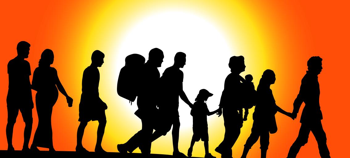 Silhouette of people walking in a line against an orange sky and bright sun. 